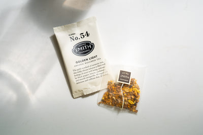 Overwrapped sachet of Golden Light beside unwrapped sachet of Golden Light to show loose tea.