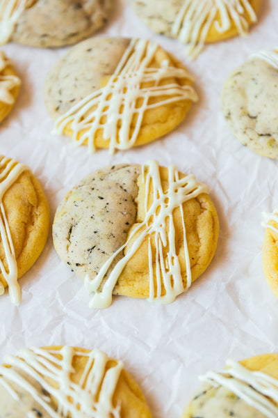 Cookies with a white icing drizzle on a white table. Cookies are half lemon, half tea based batter.