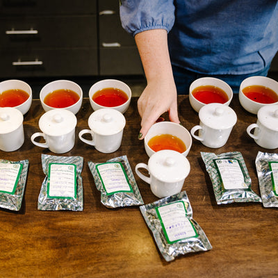 Six Gaiwan tea tasting samples and six bags of tea on dark wood table