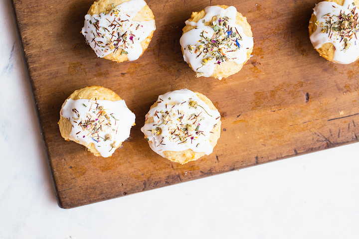 Five Meadow Honey Muffins with glaze and garnished with loose Meadow on a wooden cutting board.