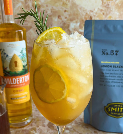 Lemon Black mocktail in wine glass with lemon slices. Wilderton Apertivo bottle and Lemon Black bag in background on marble table
