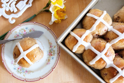 Tray of Chai and cherry hot crossed buns next to a plate with a single bun.