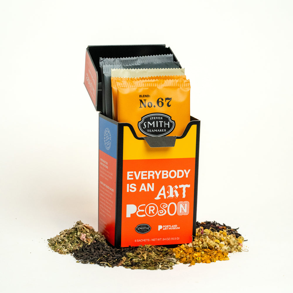 Opened red Tea Gallery carton against a white background with piles of loose tea around it to show sachets inside.