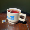 White mug with 'Art Person' branding filled with tea on a wooden surface