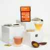 Tea Gallery carton on white blocks featuring cups of tea, loose sachets, loose tea and a wooden spoon filled with tea.