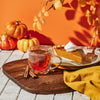 Clear mug filled with Autumn Leaves hot tea on a wooden tray with a piece of pumpkin pie and pumpkins in the background.