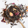 Upclose of a spoon filled with loose tea to show black tea leaves, rose petals and sarsaparilla.