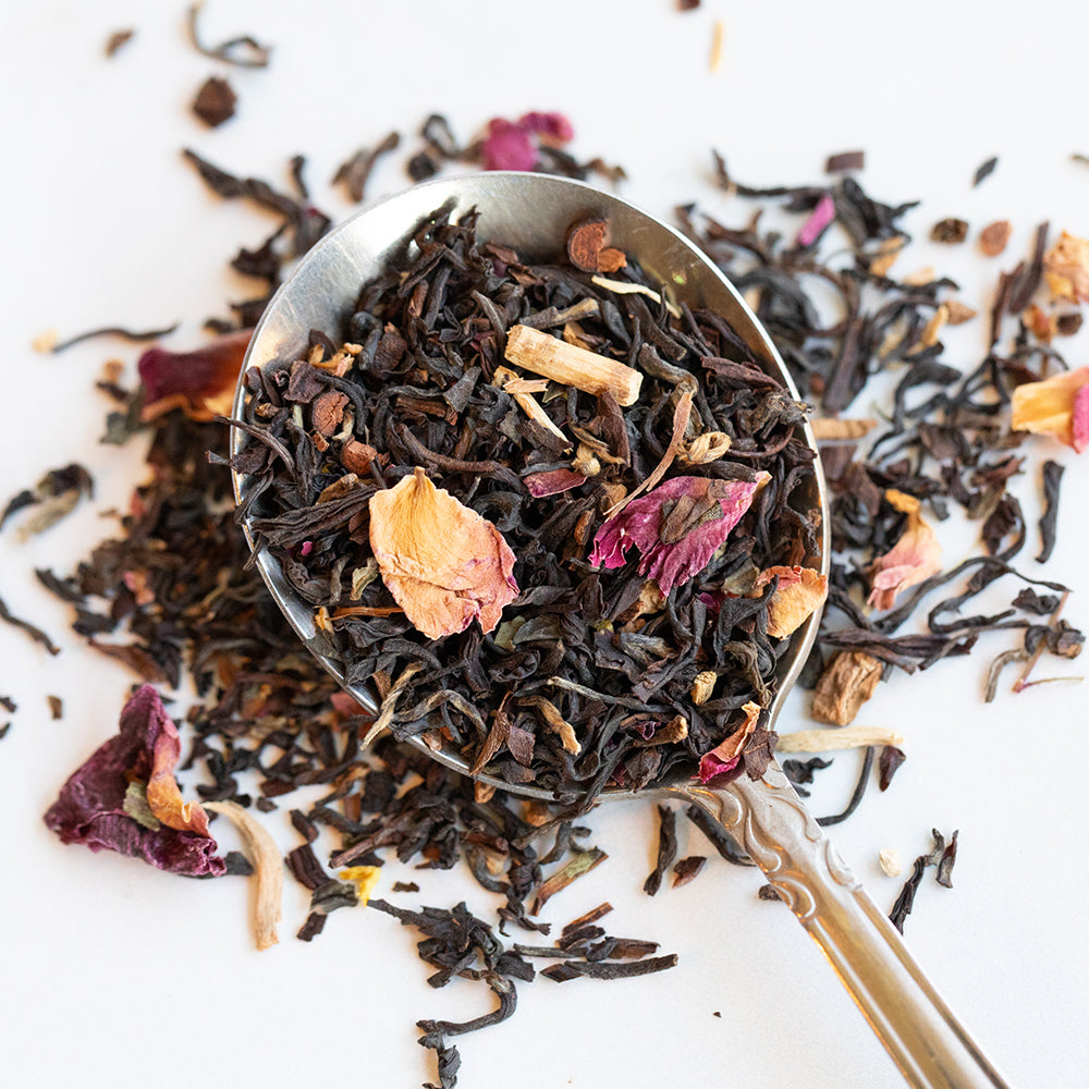 Upclose of a spoon filled with loose tea to show black tea leaves, rose petals and sarsaparilla.