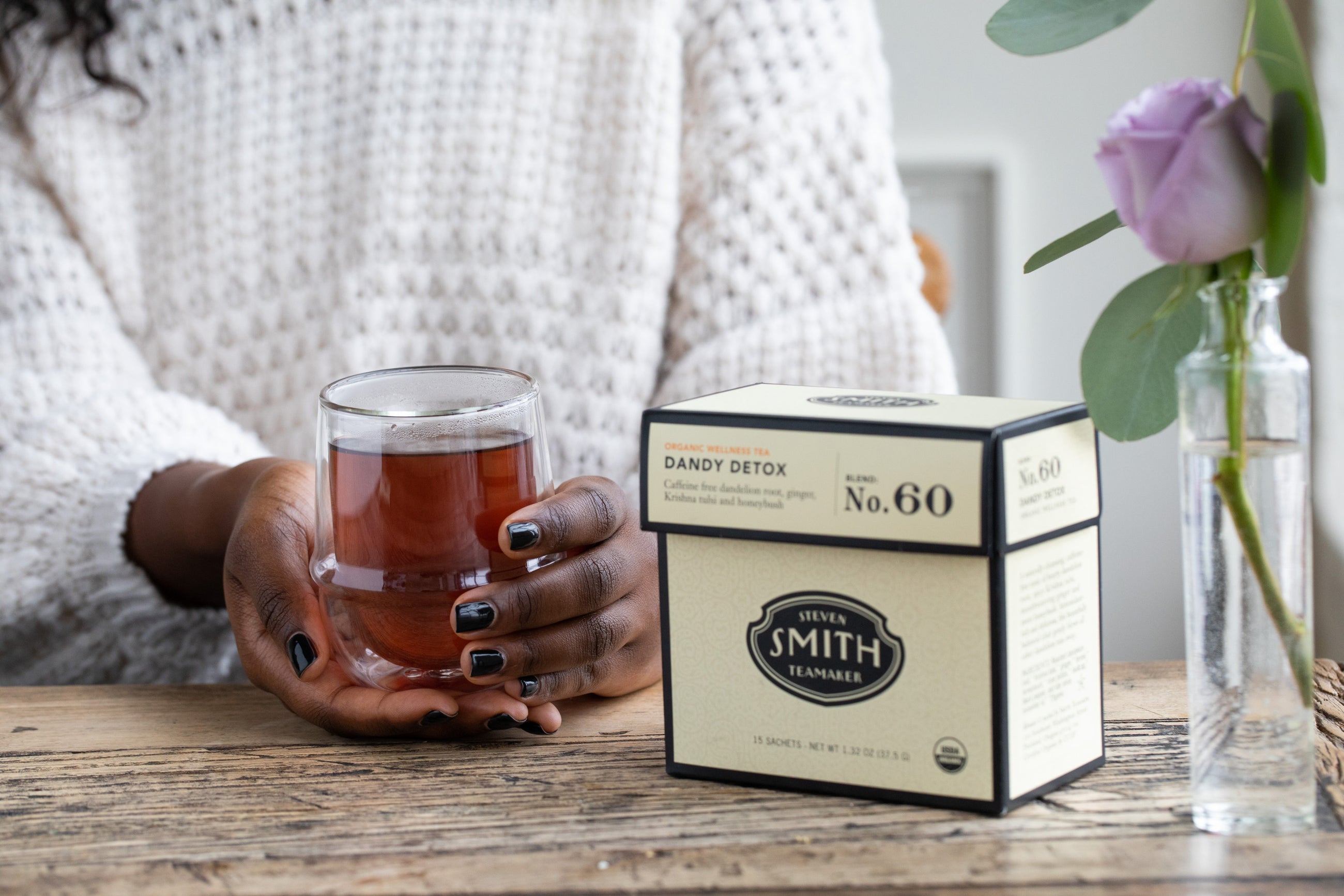 A cream colored box of Dandy Detox beside a person holding a glass mug filled with tea.