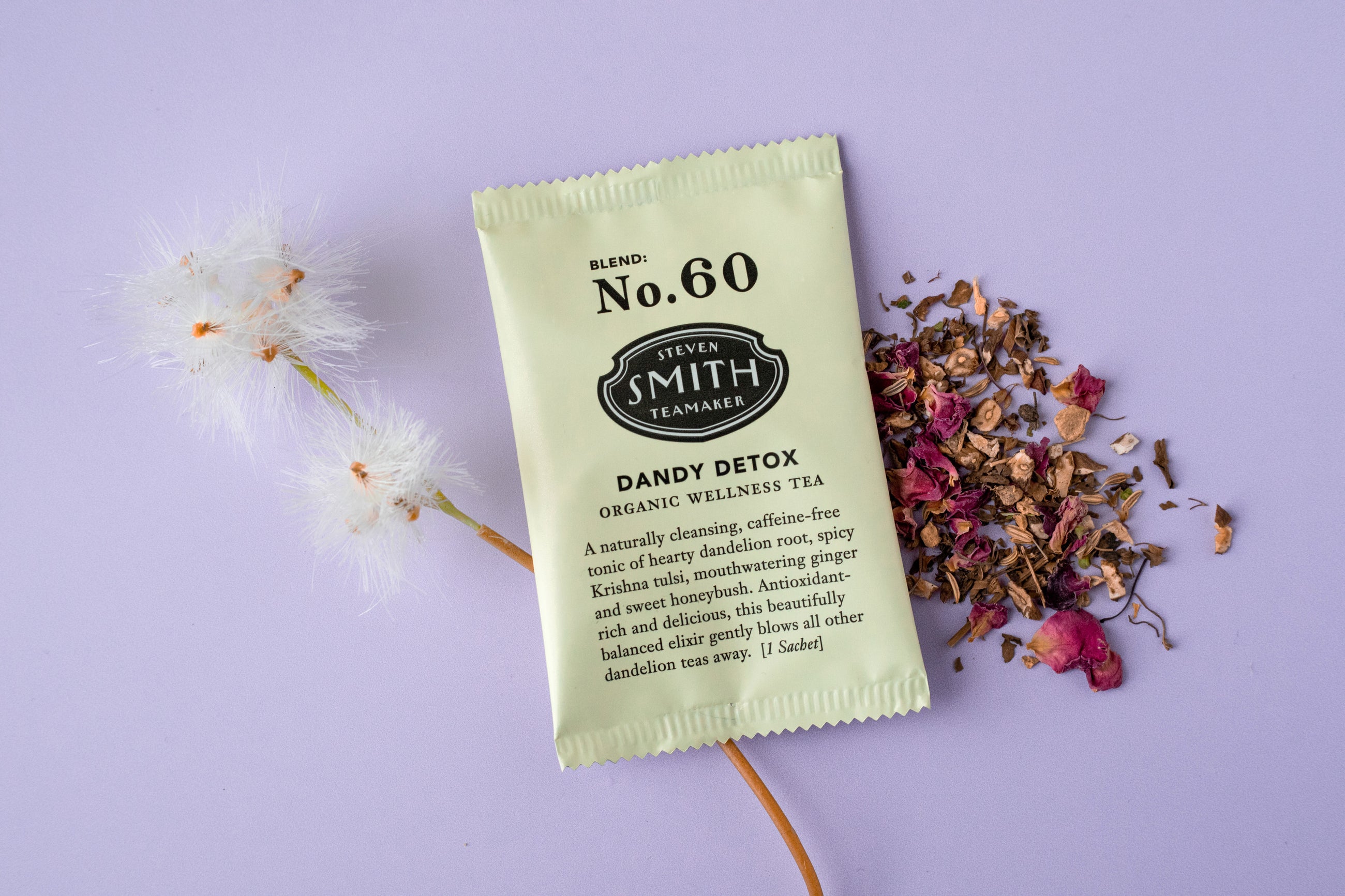 Overwrapped sachet of Dandy Detox with cream packaging and loose tea on purple background.