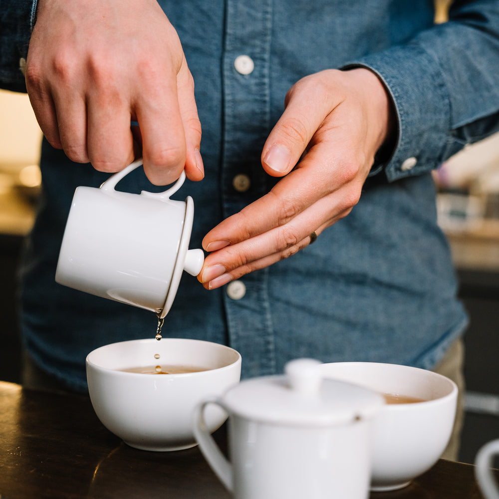 Hands holding tea strainer above sample cup to show straining tea.