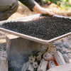 Sheet tray filled with loose leaf oolong tea gently placed over a charcoal fire in the woods.