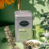 Grey tin of Garden Party with a green label and black Smith Teamaker logo in a green, flower filled background.