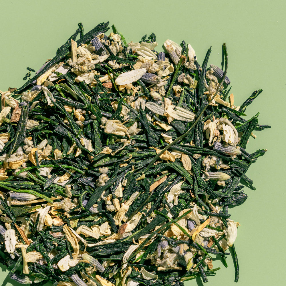 Pile of loose leaf Garden Party green tea to show gyokuro green tea, lavender, hyssop and chamomile against a green background.