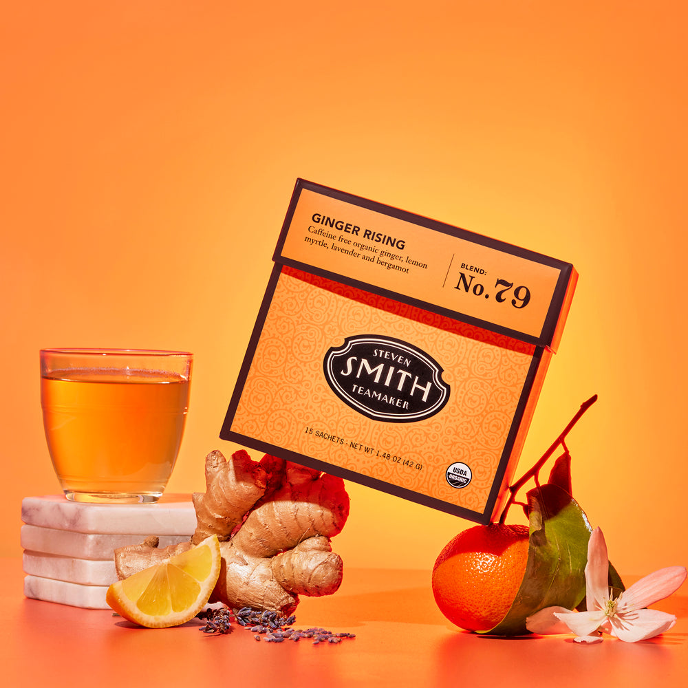 Orange tea package with a glass of tea, ginger root, lemon and other ingredients on an orange background