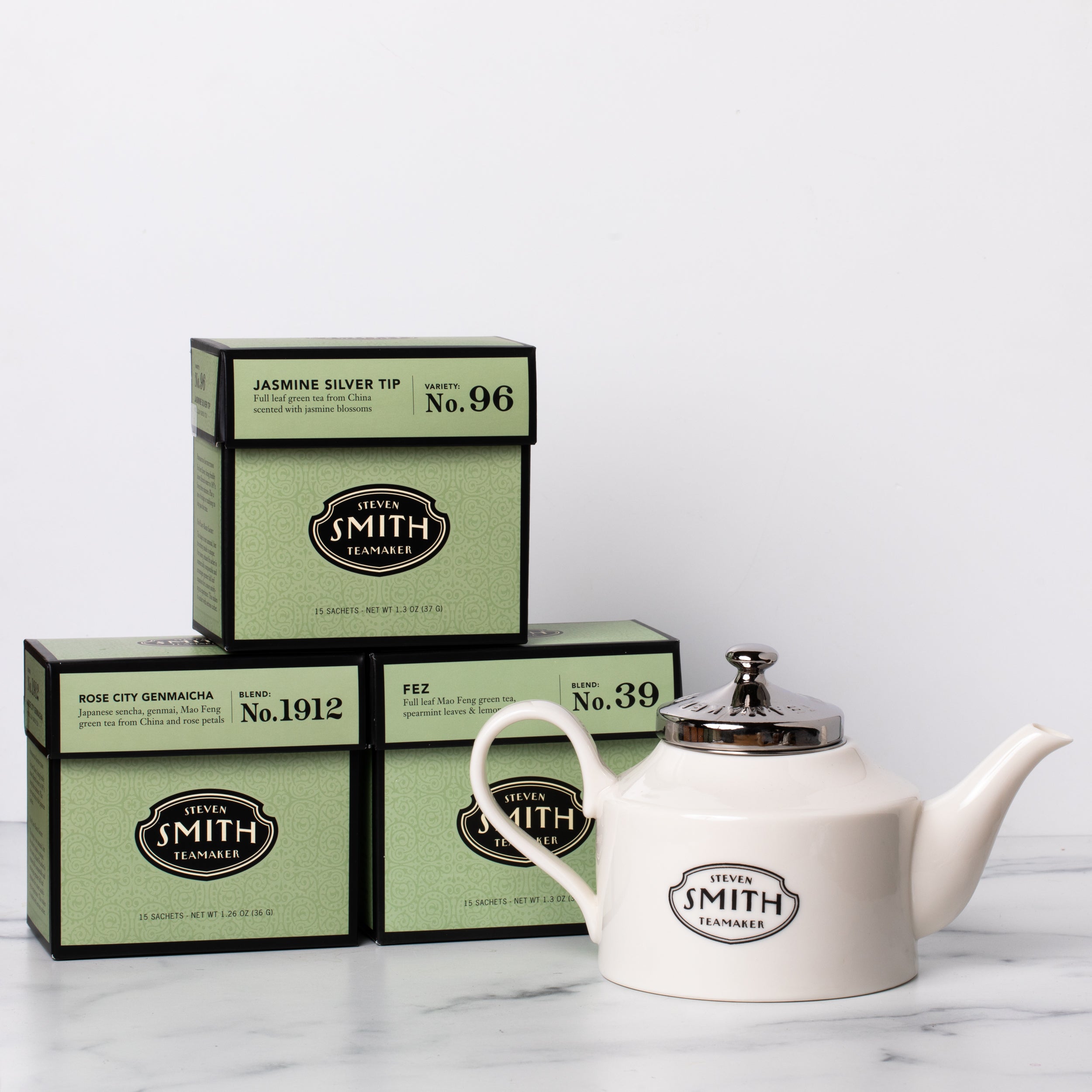 Three cartons of green tea with a white porcelain teapot.
