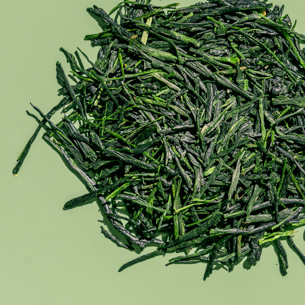 Loose leaf gyokuro green tea to show bright green, flat tea leaves against a green background.
