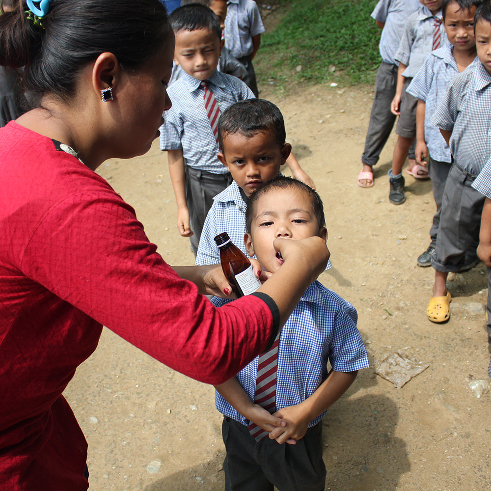 Healthcare aid administering medicine to a school boy in Darjeeling, India.