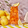 Tall glass filled with iced and Lemon Black iced tea garnished with a lemon wedge on a table with a basket of lemons.