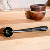Loose tea scoop on wooden counter with stacked teacups.