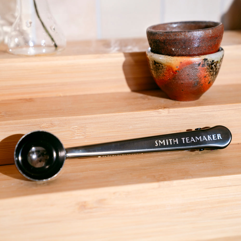 Loose tea scoop on wooden counter with stacked teacups.