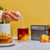 Person pouring cream into a cup of brewed Lord Bergamot black tea in a breakfast table scene with a box of Lord Bergamot.