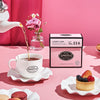 Pink box of Lover's Leap tea beside a tea cup being filled with tea on a pink table with treats.