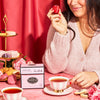 Women holding a macaron with a cup of tea and a box of Lover's Leap.