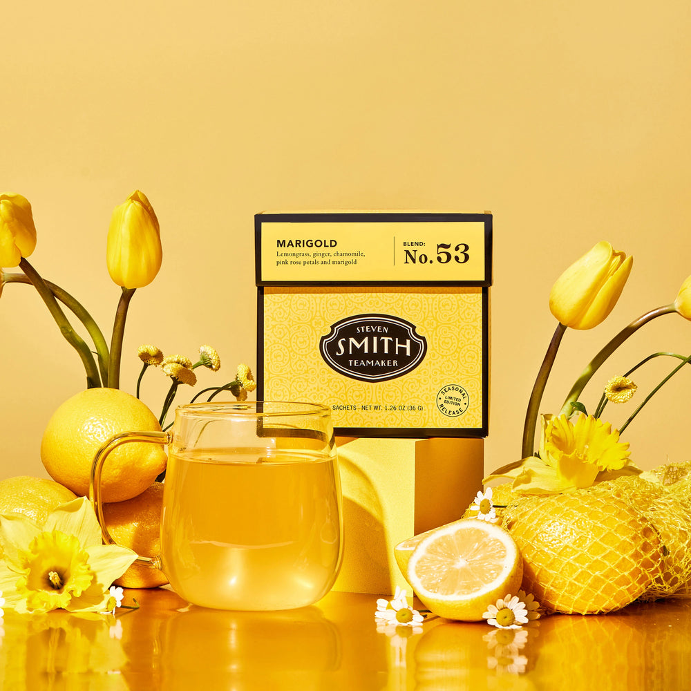 Yellow Marigold carton with brewed tea in clear glass cup with yellow backdrop and yellow tulips, daffodils, chamomile flowers and lemons in backgournd. 