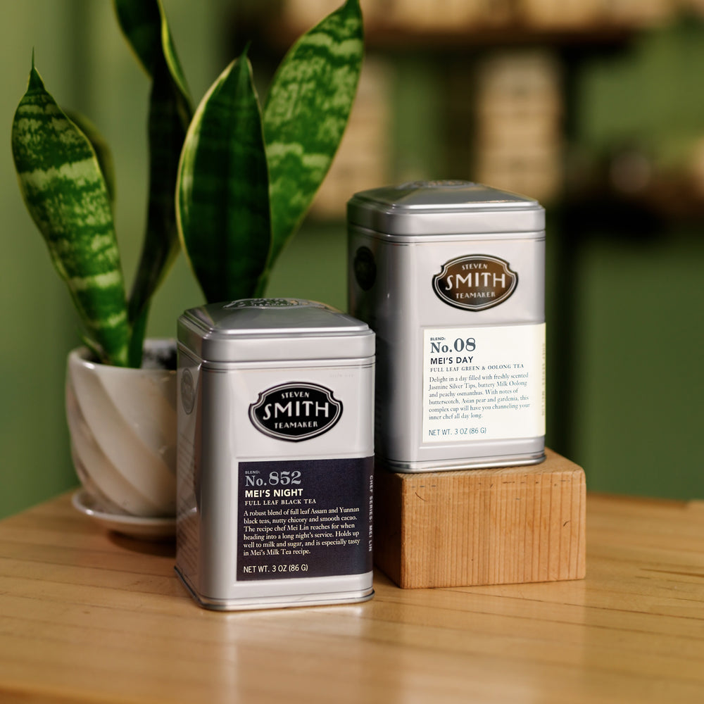 One silver tin of Mei's Day and one silver tin ofMei's Night on a wooden table.