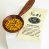 Wooden spoon filled with loose Golden Light infusion to show ingredient detail like golden turmeric and black pepper next to a wrapped sachet of Golden Light.