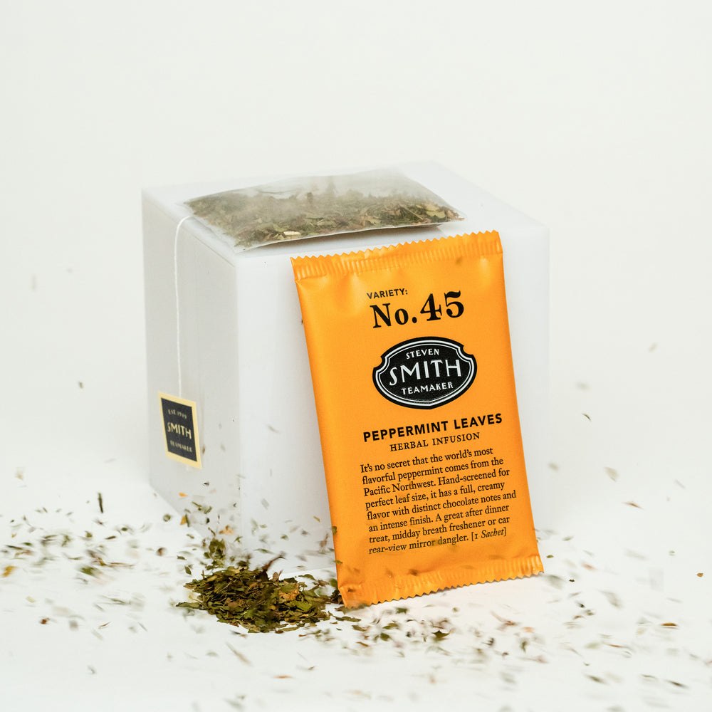 Orange wrapped sachet of Peppermint Leaves leaned againsy a small white block surrounded by loose peppermint.