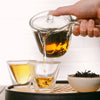 Hand pouring brewed Phoenix Oolong from an Eastern-style glass teapot into two small glass cups.
