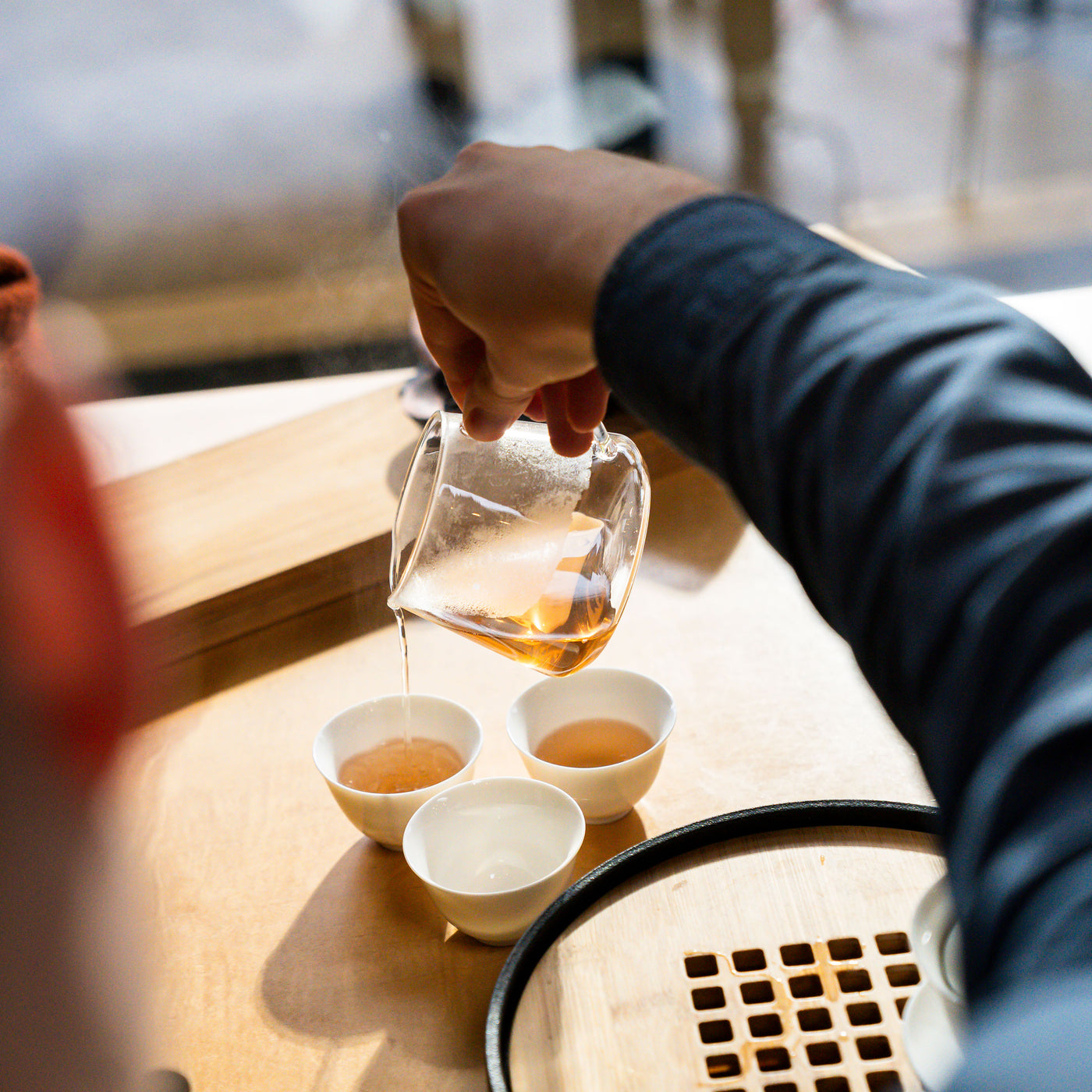 Hand pouring tea from glass tea pot into three white porcelain cups.