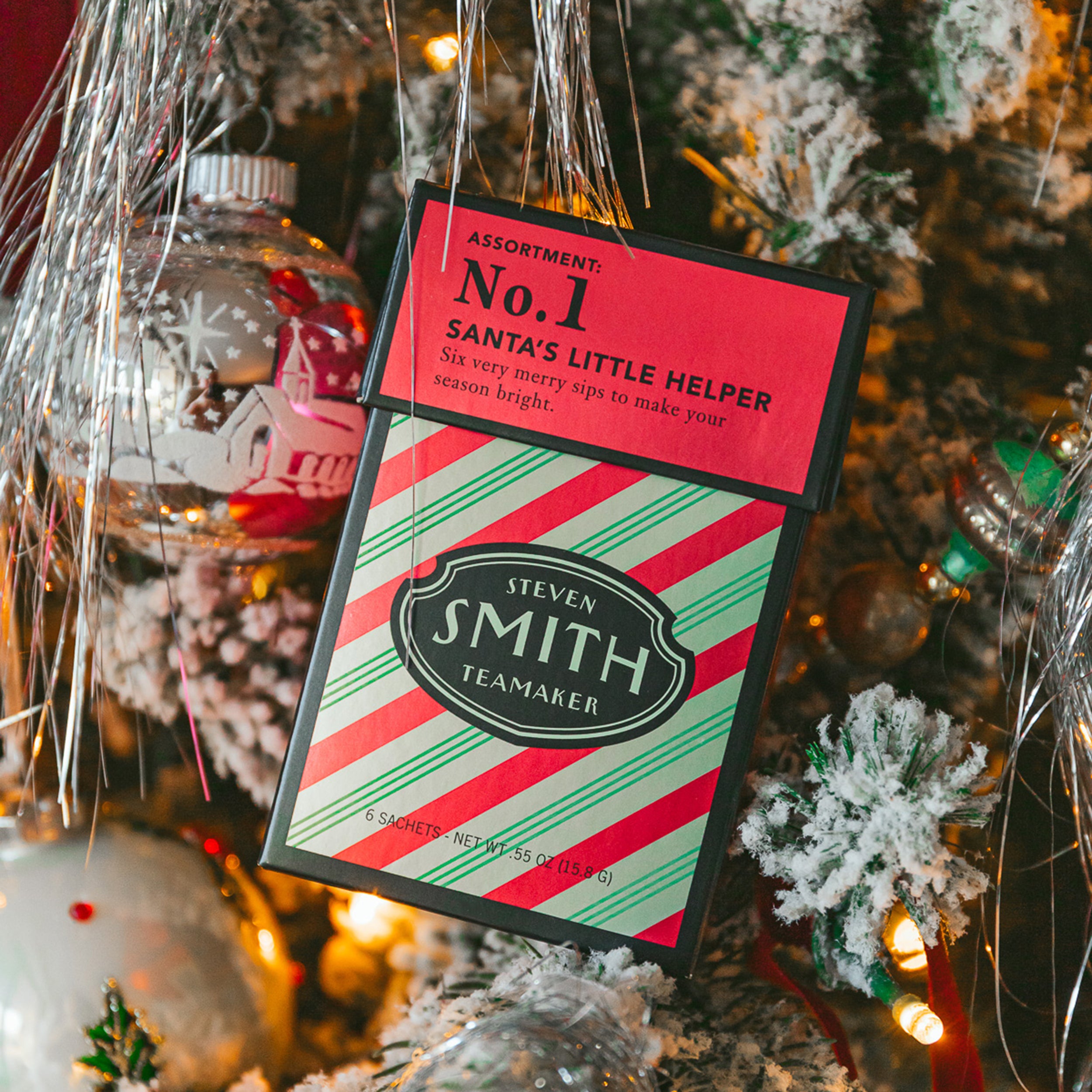 Santa's Little Helper in a festive mini carton with a red top and red and green striped base against a Christmas tree.