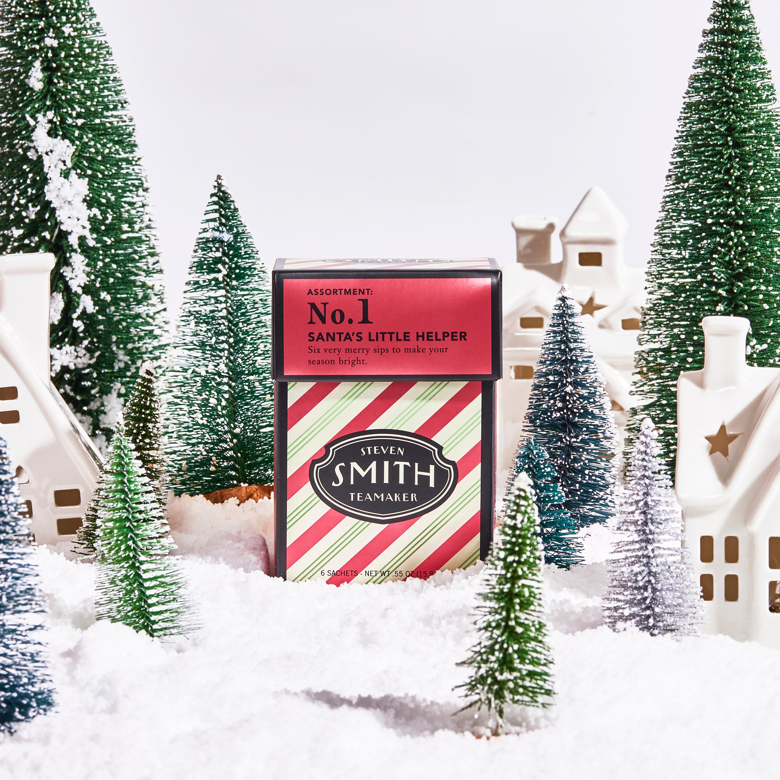 Red and green striped mini carton of Santa's Little Helper in a whimsical toy winter scene with toy trees and houses covered in prop snow.