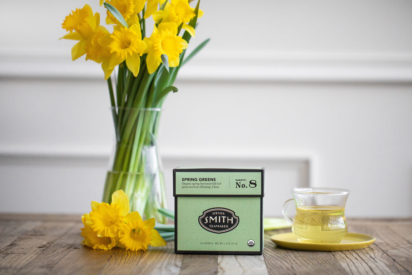 Box of Spring Greens green tea next to vase of dandelions and a brewed cup of tea.