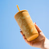 Hand holding a yellow tumbler with floral designs against a clear blue sky