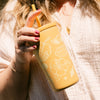 Person holding a yellow tumbler with straw with floral designs.