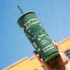 Green tumbler with branding held against a blue sky