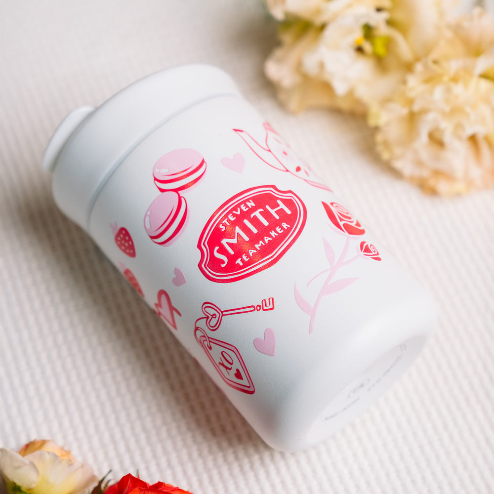 Small white beverage tumbler with a flip lid and pink Valentine's Day design with Smith logo in the middle.