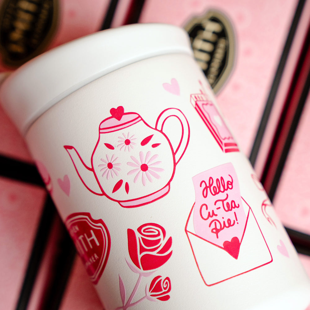 Small white beverage tumbler turned to show pink Valentine's Day design with teapot image, envelope with a love note and roses.