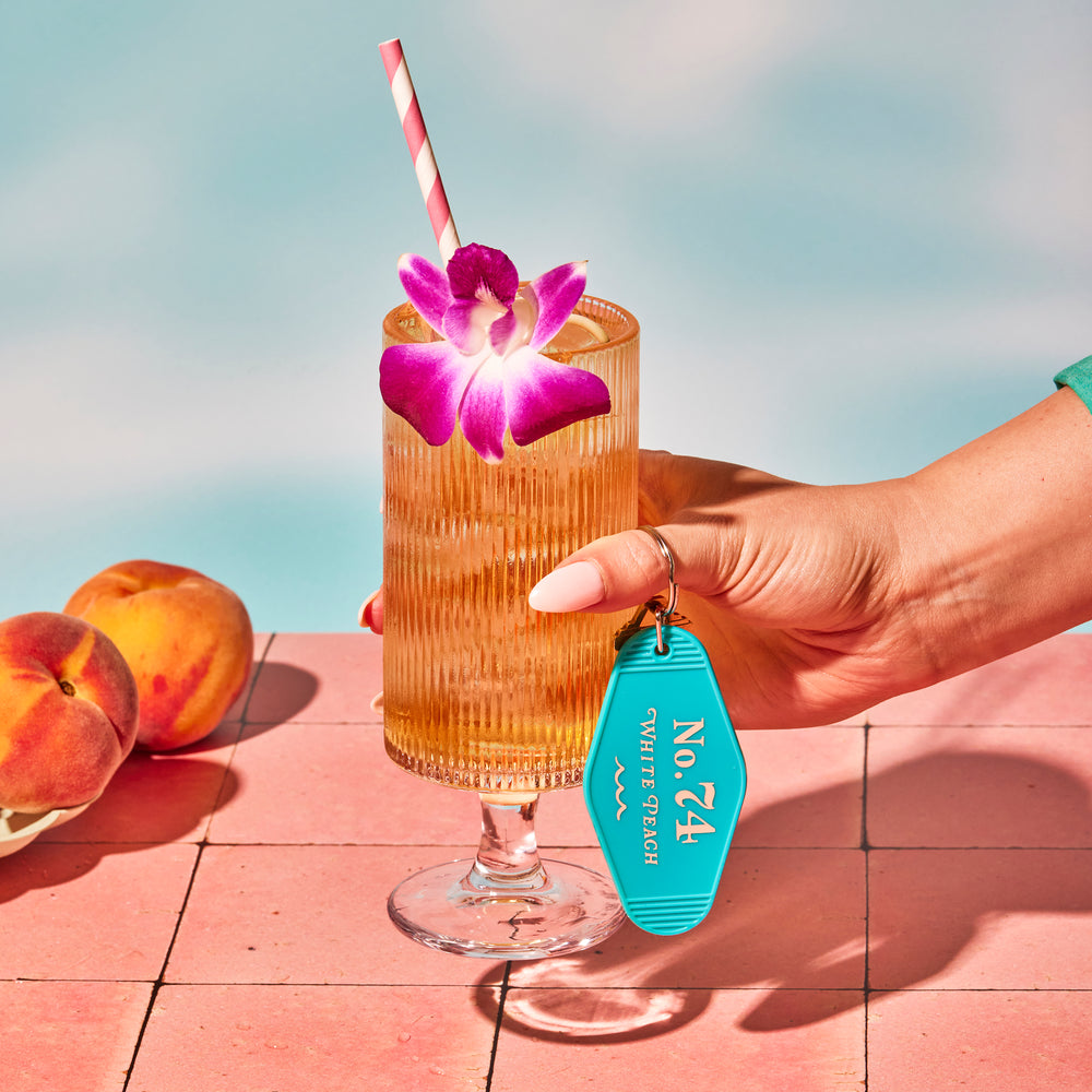 White Peach iced tea in stemmed glassware with flower and straw with a pool backdrop and peaches