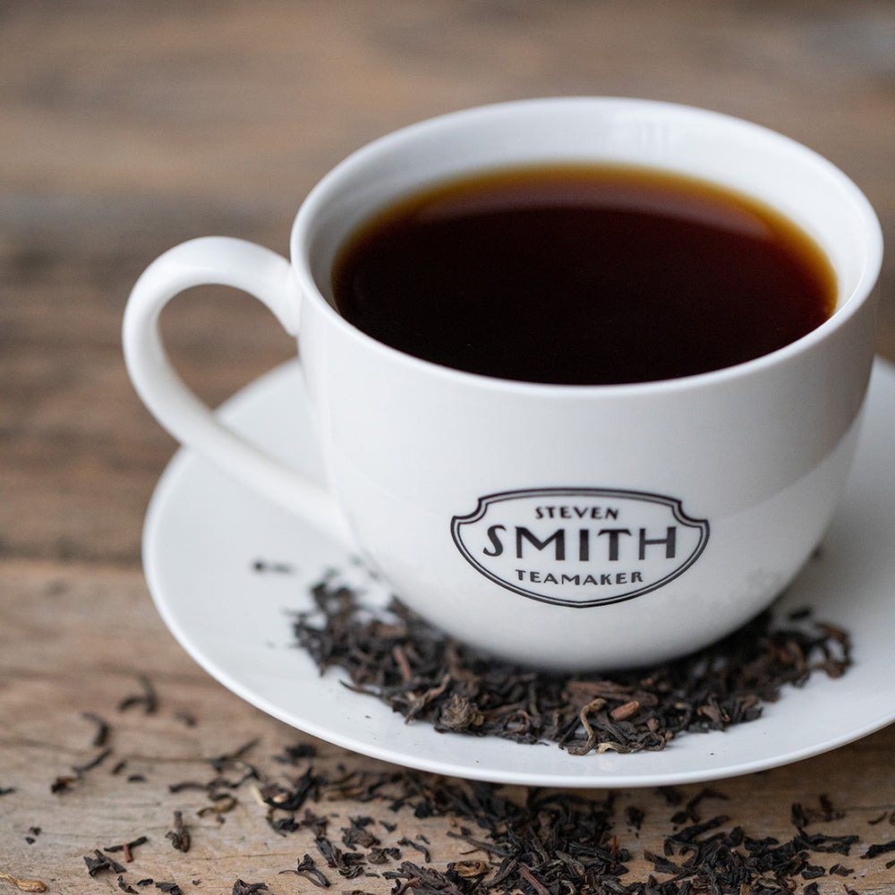 White tea cup filled with black tea sitting on a white saucer with full leaf black tea.