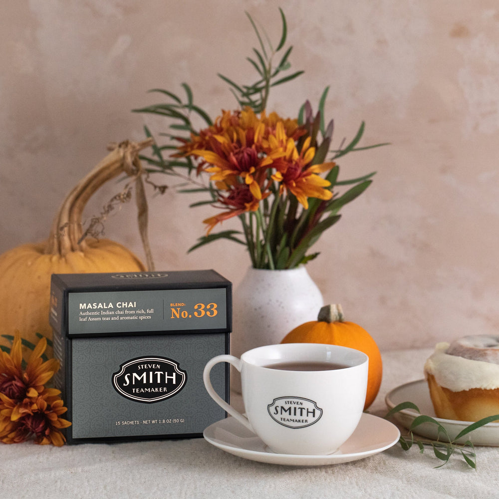 Black box of Masala Chai tea on a table with orange flowers and pumpkins.