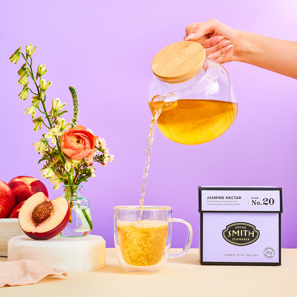 Person pouring glass teapot filled with golden jasmine nectar green tea.