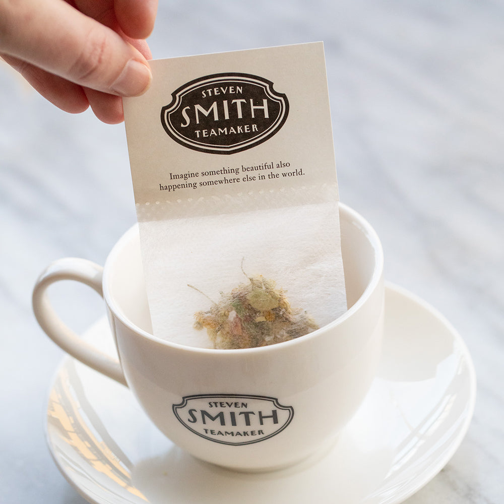 Person holding tea filter in white porcelain cup.