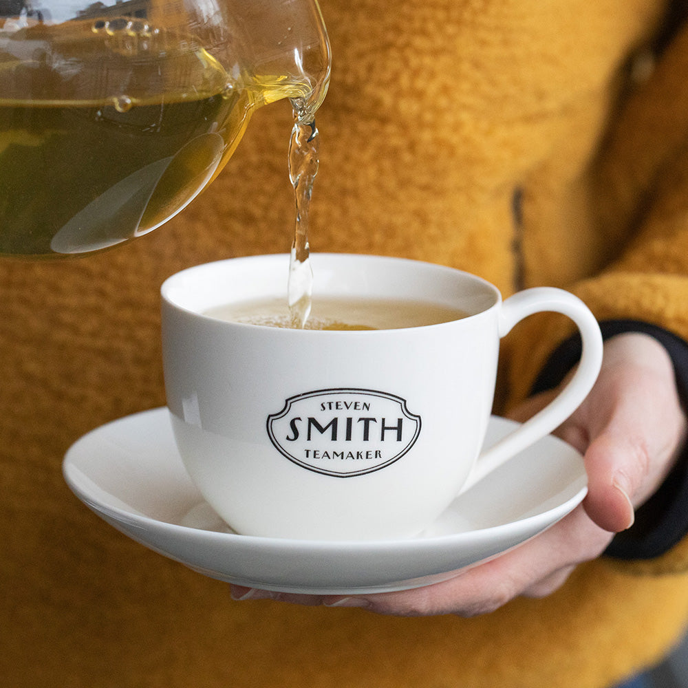 Person in an orange sweater pouring tea into white porcelain cup.