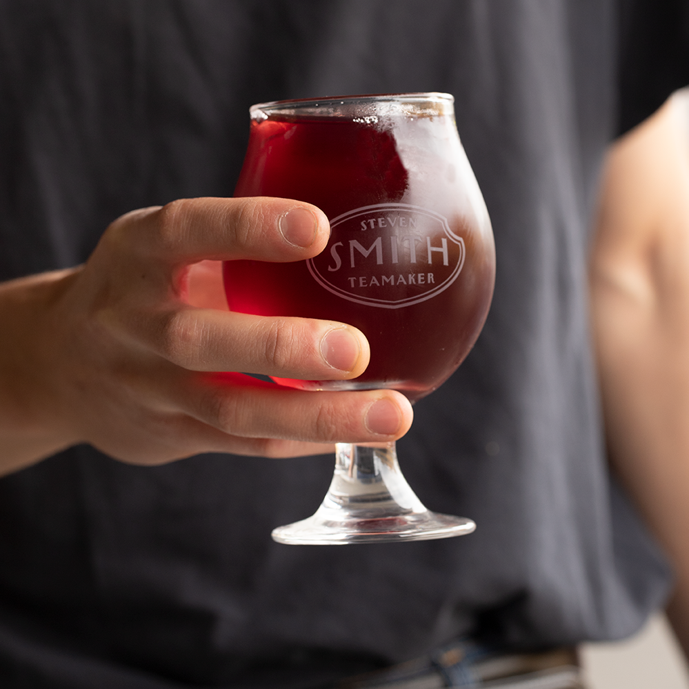 Person in black t shirt holding snifter glass filled with red iced tea.
